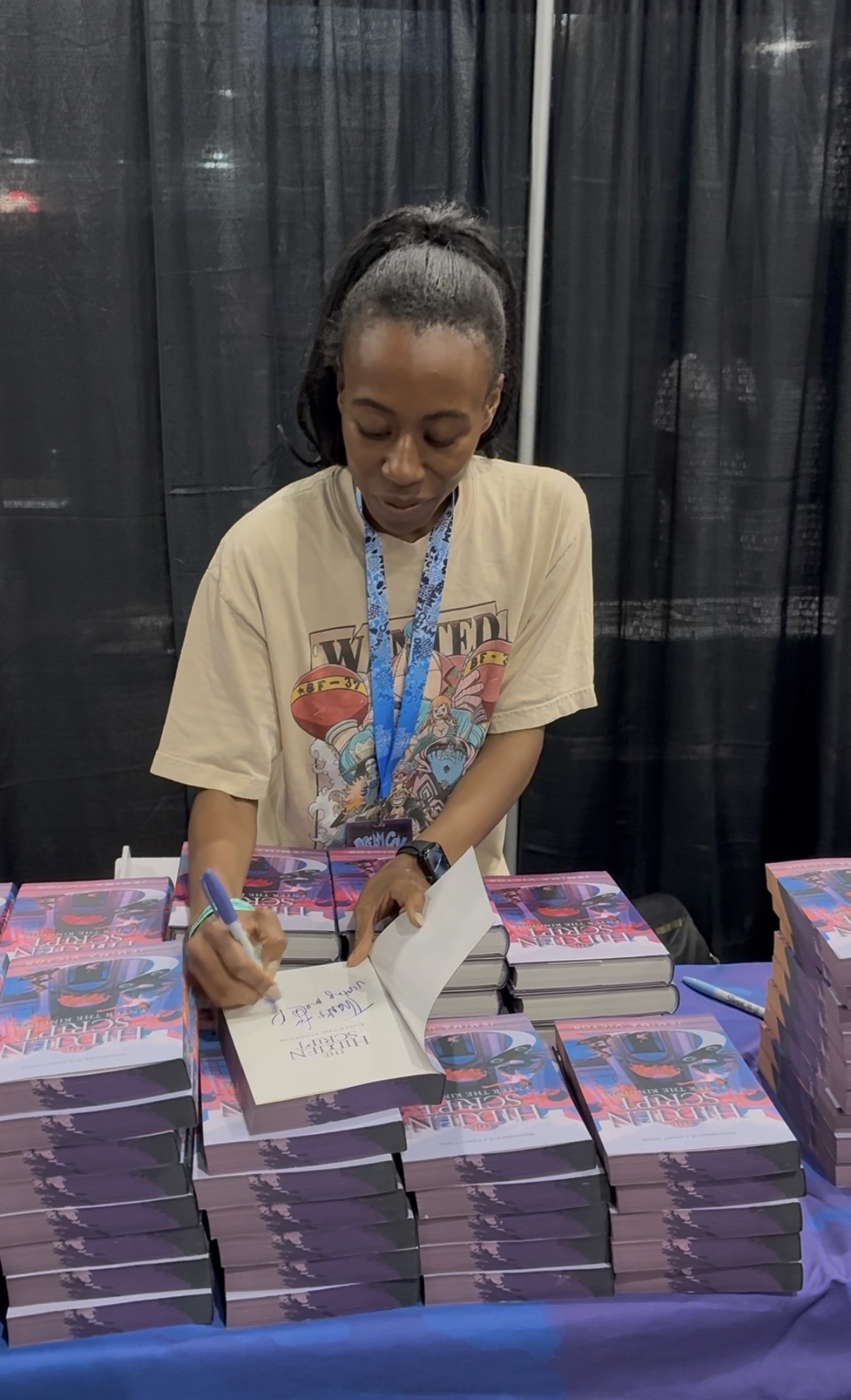 Jemima signing books with a large stack of finished copies on the table